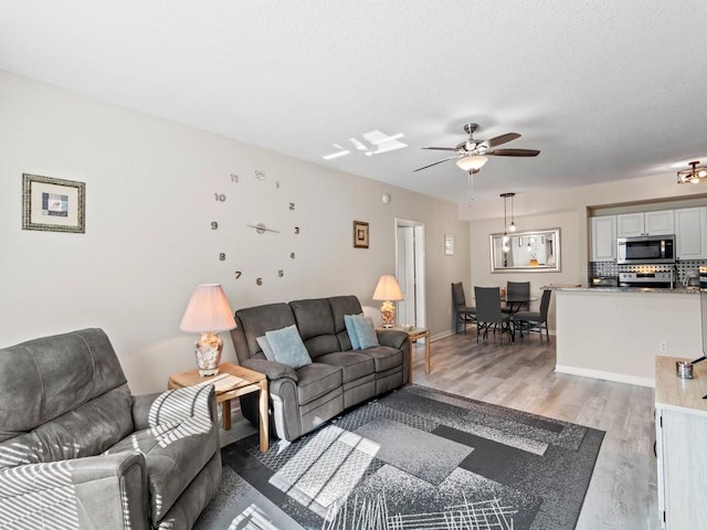 living area with a textured ceiling, baseboards, light wood finished floors, and ceiling fan