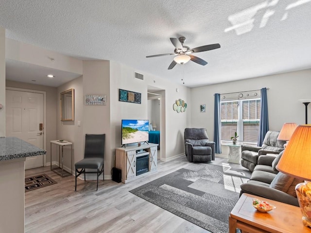 living area featuring ceiling fan, visible vents, a textured ceiling, and light wood-style flooring