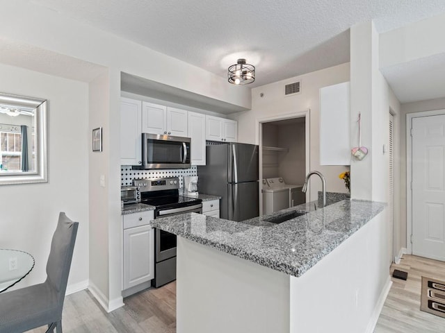 kitchen featuring appliances with stainless steel finishes, white cabinets, a peninsula, washer and dryer, and a sink