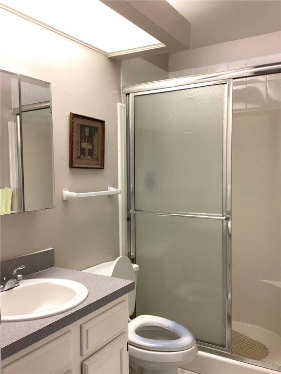 bathroom featuring a shower with shower door, vanity, and toilet