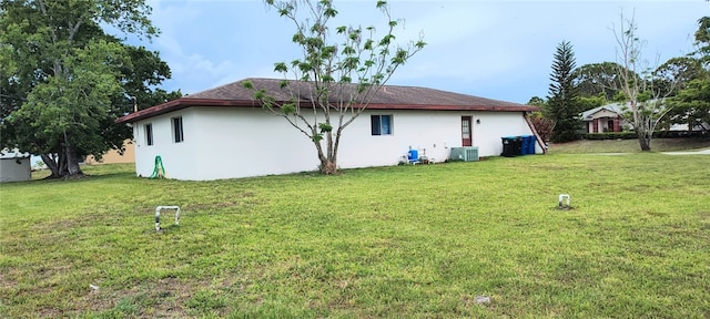 view of side of home featuring stucco siding, a yard, and cooling unit