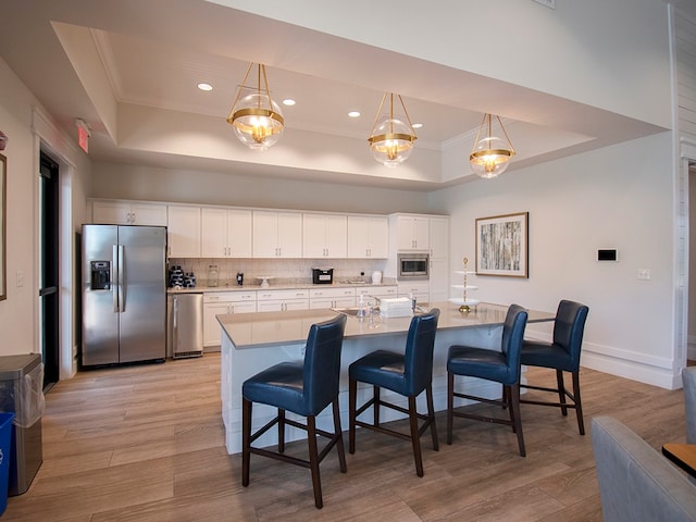 kitchen featuring white cabinets, appliances with stainless steel finishes, light wood-type flooring, and a tray ceiling