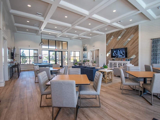 dining area with light hardwood / wood-style flooring, a towering ceiling, and a healthy amount of sunlight