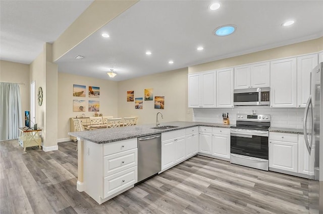 kitchen featuring a sink, appliances with stainless steel finishes, a peninsula, light wood finished floors, and decorative backsplash