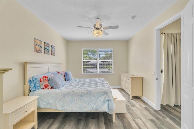 bedroom featuring light wood-style flooring, a textured ceiling, baseboards, and ceiling fan