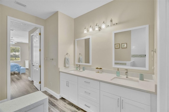 ensuite bathroom with a sink, visible vents, wood finished floors, and double vanity