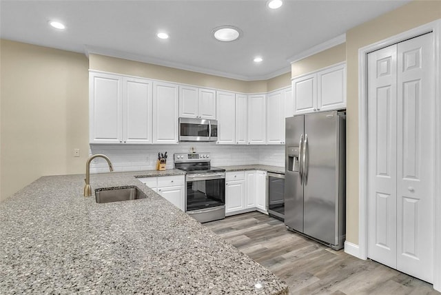 kitchen with light stone countertops, light wood-style flooring, a sink, stainless steel appliances, and white cabinets