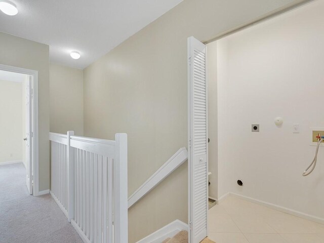 corridor featuring light tile patterned flooring, baseboards, light colored carpet, and an upstairs landing