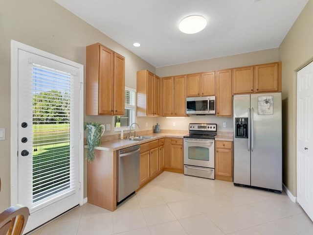 kitchen with light brown cabinets, stainless steel appliances, a sink, baseboards, and light countertops