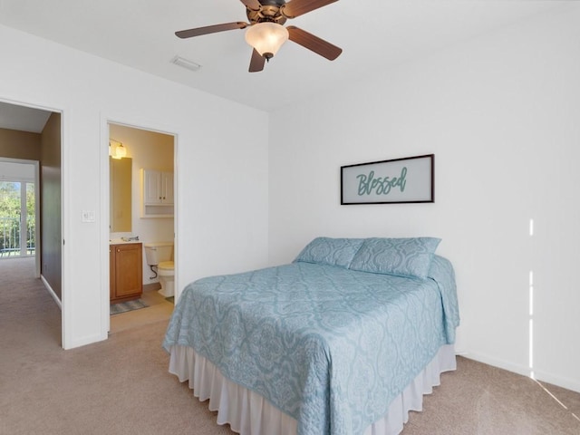 bedroom featuring ceiling fan, light colored carpet, and ensuite bath