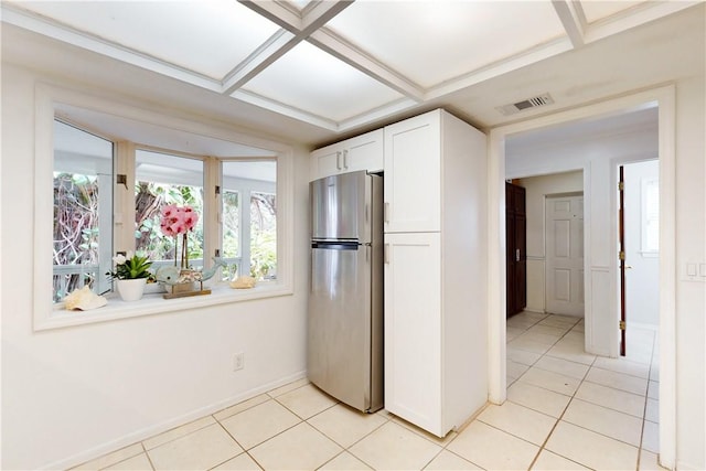 kitchen featuring coffered ceiling, light tile patterned floors, stainless steel fridge, and white cabinets