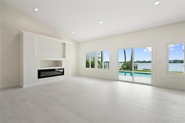 9670 Riverview Dr, Micco, FL 32976 - unfurnished living room featuring healthy amount of natural light, a glass covered fireplace, wood finished floors, vaulted ceiling, and recessed lighting