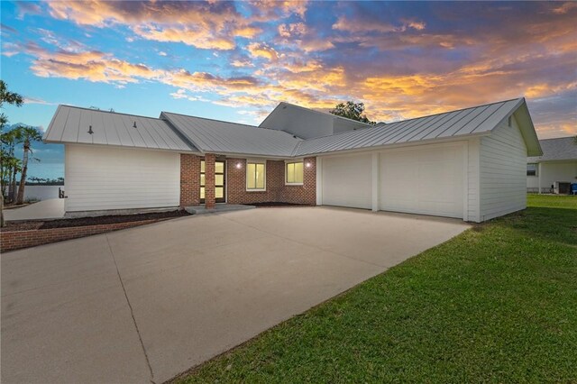9670 Riverview Dr, Micco, FL 32976 - view of front of home with an attached garage, a metal roof, driveway, a yard, and a standing seam roof