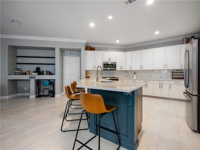 kitchen featuring stainless steel appliances, white cabinetry, a breakfast bar, built in shelves, and a kitchen island with sink