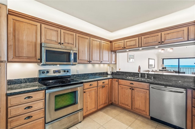 kitchen with stainless steel appliances, dark stone counters, sink, and light tile patterned flooring