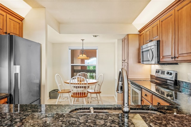 kitchen with stainless steel appliances, dark stone counters, sink, light tile patterned flooring, and pendant lighting