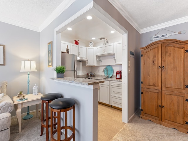 kitchen featuring a breakfast bar, ornamental molding, a textured ceiling, white cabinets, and stainless steel fridge