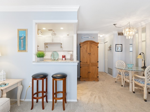 kitchen featuring light stone counters, ornamental molding, white cabinetry, an inviting chandelier, and light colored carpet