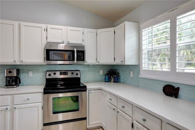 kitchen with white cabinets, appliances with stainless steel finishes, tasteful backsplash, and vaulted ceiling