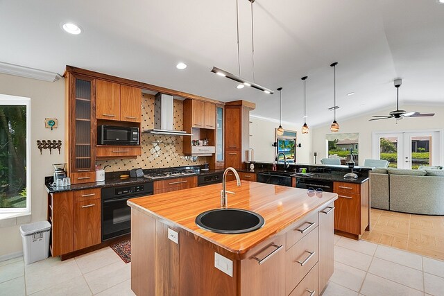 kitchen featuring vaulted ceiling, wall chimney exhaust hood, black appliances, a kitchen island with sink, and pendant lighting