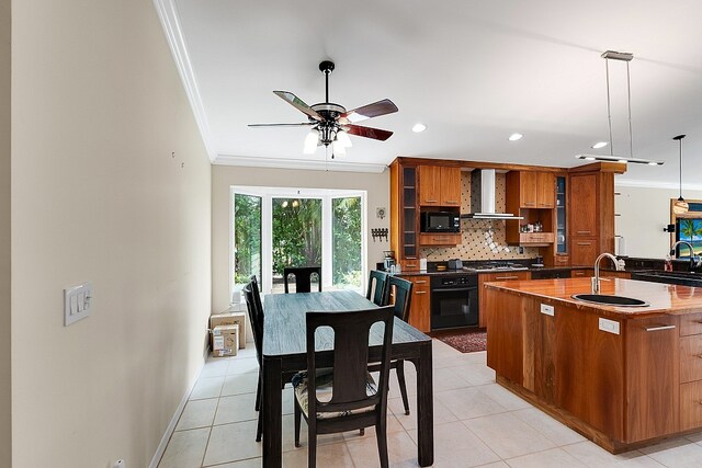 kitchen featuring hanging light fixtures, black appliances, sink, an island with sink, and wall chimney range hood