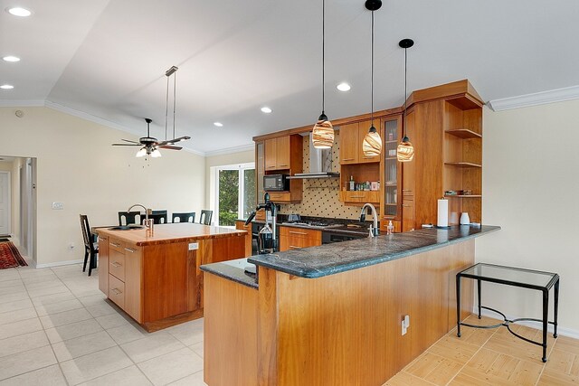 kitchen featuring kitchen peninsula, hanging light fixtures, a kitchen island with sink, ornamental molding, and wall chimney range hood