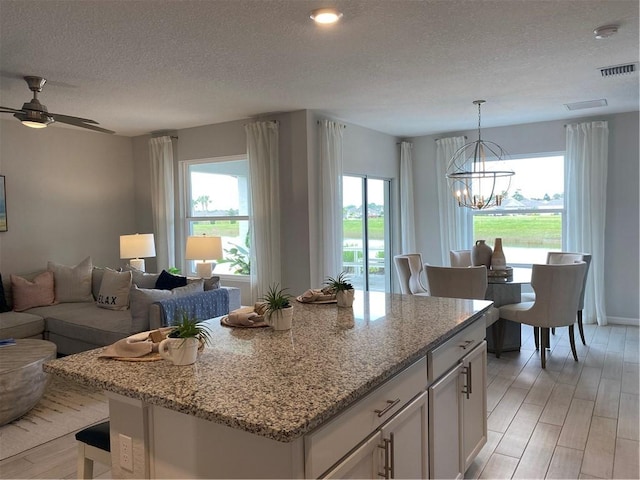 kitchen with white cabinetry, hanging light fixtures, light stone counters, and a textured ceiling