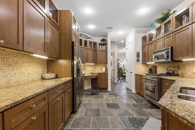 kitchen with appliances with stainless steel finishes, a textured ceiling, light stone counters, and backsplash