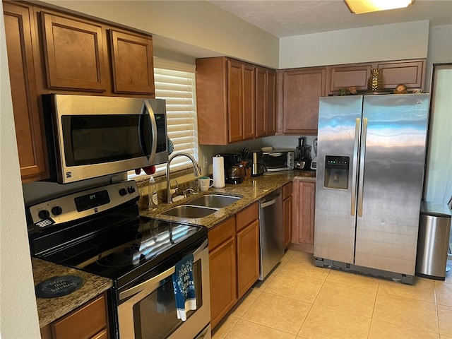 kitchen featuring sink, light tile patterned flooring, dark stone counters, and appliances with stainless steel finishes