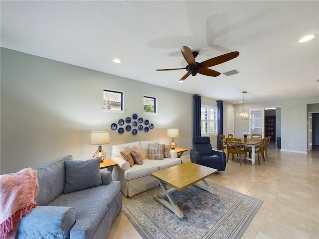 living room featuring ceiling fan with notable chandelier, a textured ceiling, and light tile patterned floors