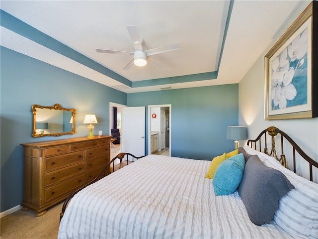 bedroom with a raised ceiling, light carpet, ceiling fan, and ensuite bathroom