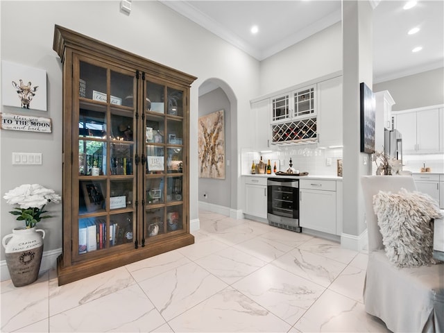 bar with tasteful backsplash, beverage cooler, ornamental molding, and white cabinets