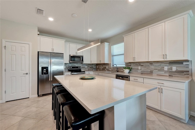 kitchen with a breakfast bar, hanging light fixtures, appliances with stainless steel finishes, a kitchen island, and white cabinetry