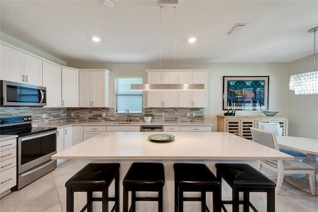 kitchen with white cabinetry, a center island, pendant lighting, a kitchen bar, and appliances with stainless steel finishes