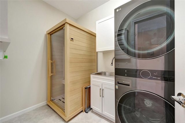 laundry room featuring cabinets, sink, light tile patterned floors, and stacked washing maching and dryer