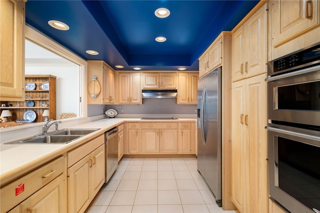 kitchen featuring light brown cabinetry, sink, light tile patterned flooring, stainless steel appliances, and a tray ceiling