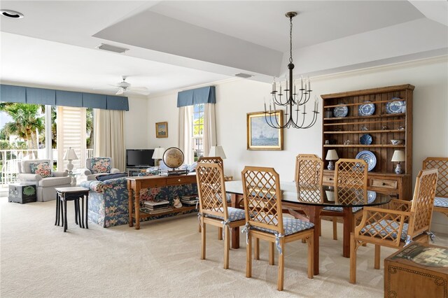 carpeted dining area featuring ceiling fan with notable chandelier, a tray ceiling, ornamental molding, and a healthy amount of sunlight