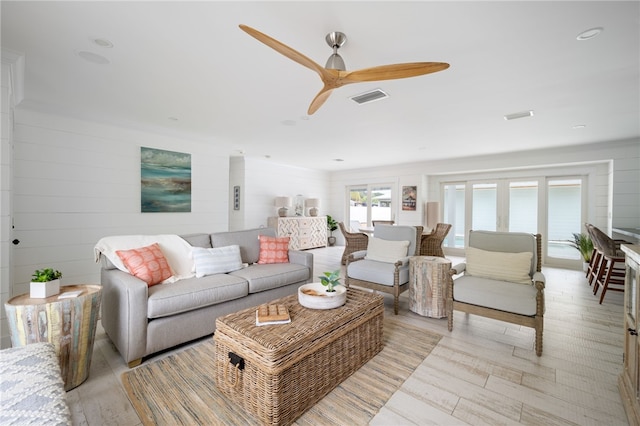 living room with light hardwood / wood-style flooring, ceiling fan, and wood walls