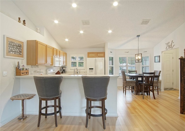 kitchen featuring kitchen peninsula, pendant lighting, vaulted ceiling, white appliances, and light wood-type flooring