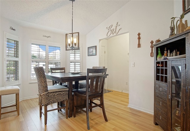 dining room with a notable chandelier, light hardwood / wood-style floors, lofted ceiling, and a textured ceiling