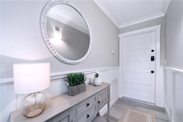 foyer featuring ornamental molding, visible vents, wainscoting, and light wood-style flooring