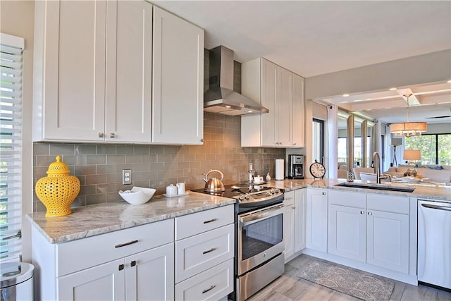 kitchen featuring decorative backsplash, appliances with stainless steel finishes, wall chimney range hood, white cabinetry, and a sink