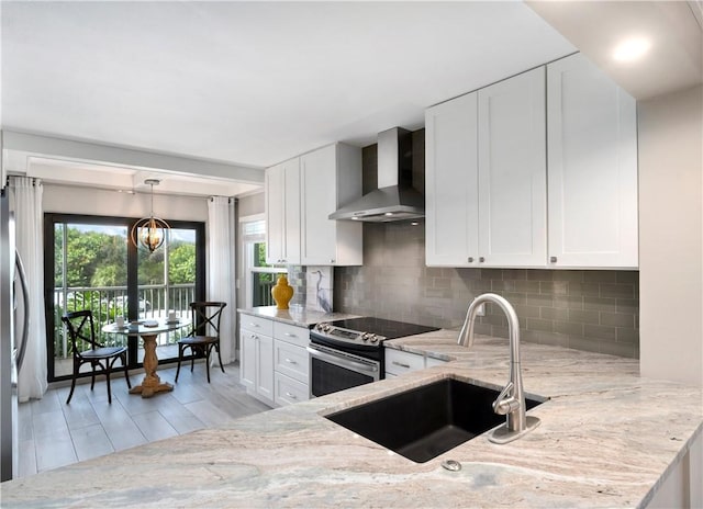 kitchen featuring light stone counters, appliances with stainless steel finishes, white cabinets, a sink, and wall chimney exhaust hood