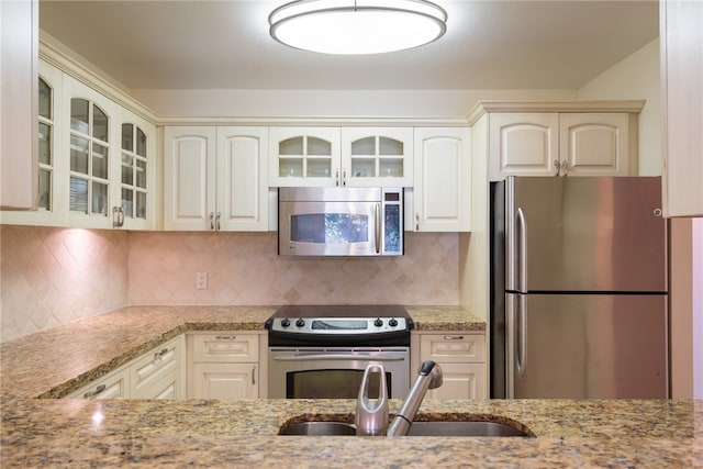 kitchen featuring stainless steel appliances, sink, light stone counters, and decorative backsplash