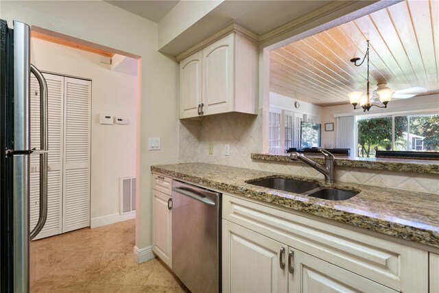 kitchen featuring light stone counters, backsplash, sink, stainless steel dishwasher, and a chandelier