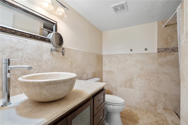 bathroom featuring toilet, vanity, tile walls, and a tile shower