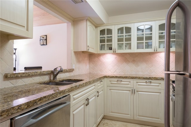 kitchen featuring stainless steel appliances, cream cabinetry, sink, light stone counters, and decorative backsplash