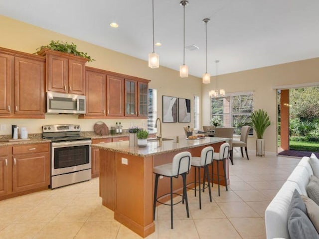 kitchen with appliances with stainless steel finishes, decorative light fixtures, sink, a kitchen island with sink, and light stone counters