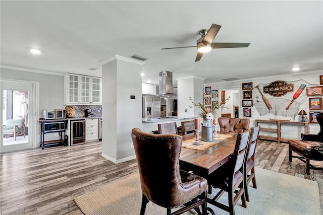 dining area with light wood-type flooring, wine cooler, ceiling fan, and ornamental molding