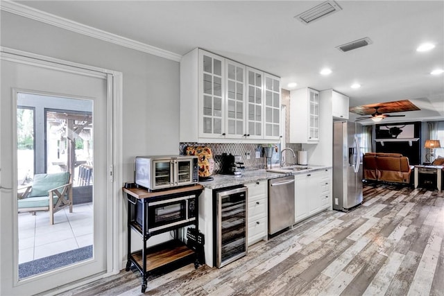 kitchen featuring appliances with stainless steel finishes, crown molding, white cabinets, light hardwood / wood-style floors, and wine cooler